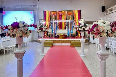 Salle de réception décorée avec des tables élégantes, des bouquets de fleurs et une estrade ornée d'un canapé doré.