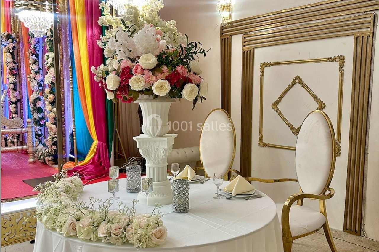 Table élégamment dressée avec des fleurs blanches et roses, entourée de décorations colorées et dorées en arrière-plan.