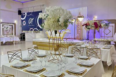Salle de réception décorée avec des tables élégantes, des bouquets de fleurs et une estrade ornée d'un canapé doré.