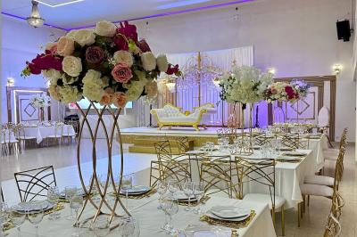 Salle de réception décorée avec des tables élégantes, des bouquets de fleurs et une estrade ornée d'un canapé doré.