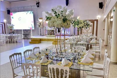 Salle de réception décorée avec des tables élégantes, des bouquets de fleurs et une estrade ornée d'un canapé doré.