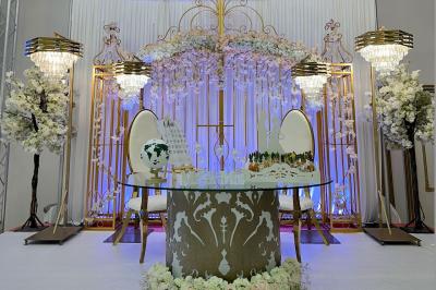 Salle de réception décorée avec des tables élégantes, des bouquets de fleurs et une estrade ornée d'un canapé doré.