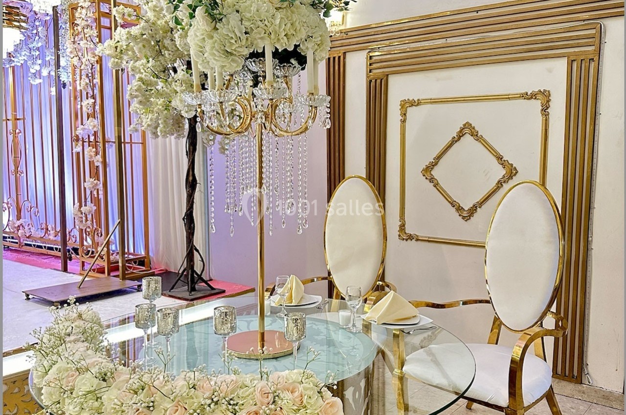 Table décorée avec des fleurs blanches et roses, chandelier doré orné de cristaux, deux chaises blanches élégantes.