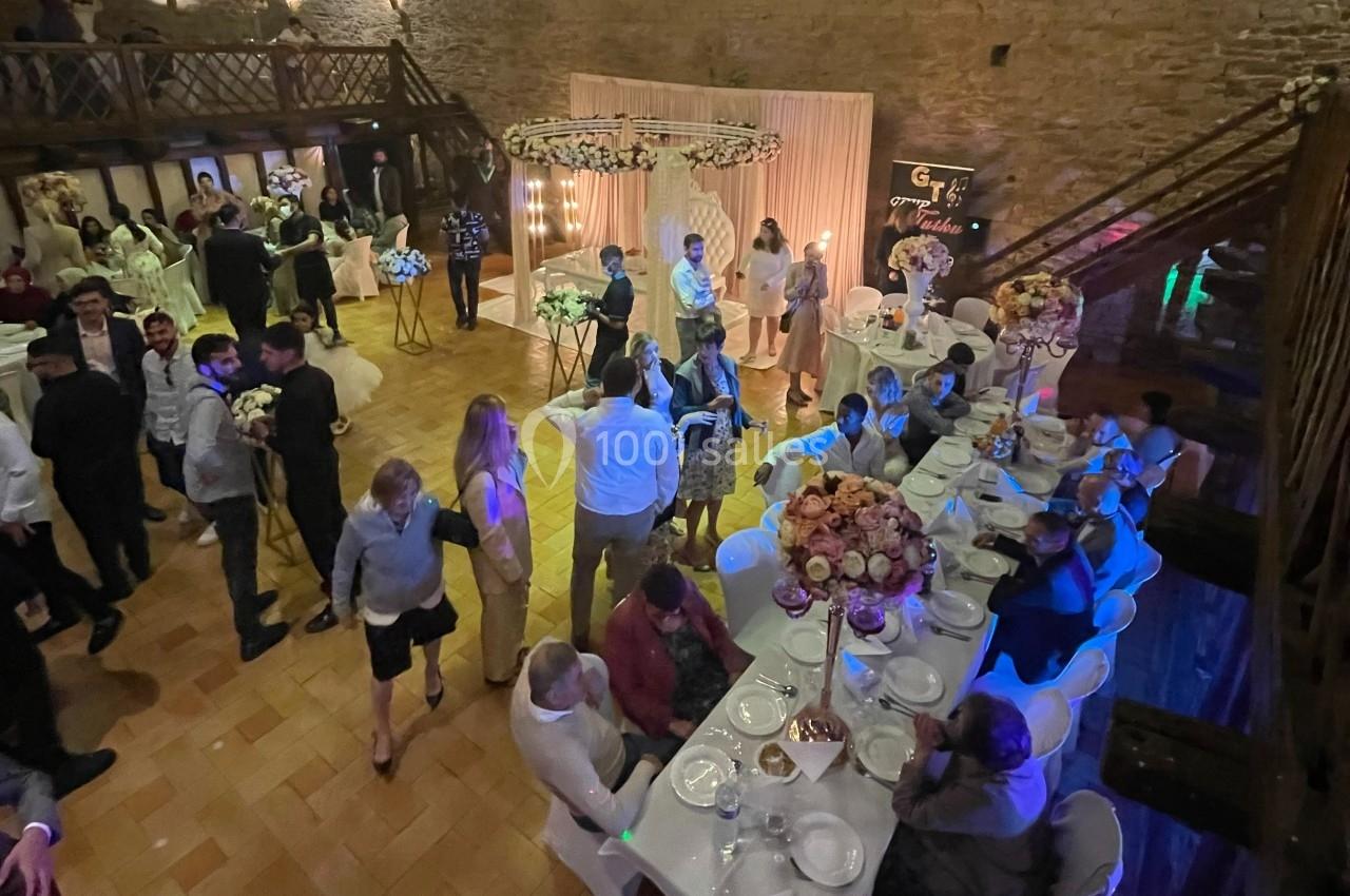 Salle de réception animée avec des invités assis et debout, décorations florales et éclairage chaleureux.