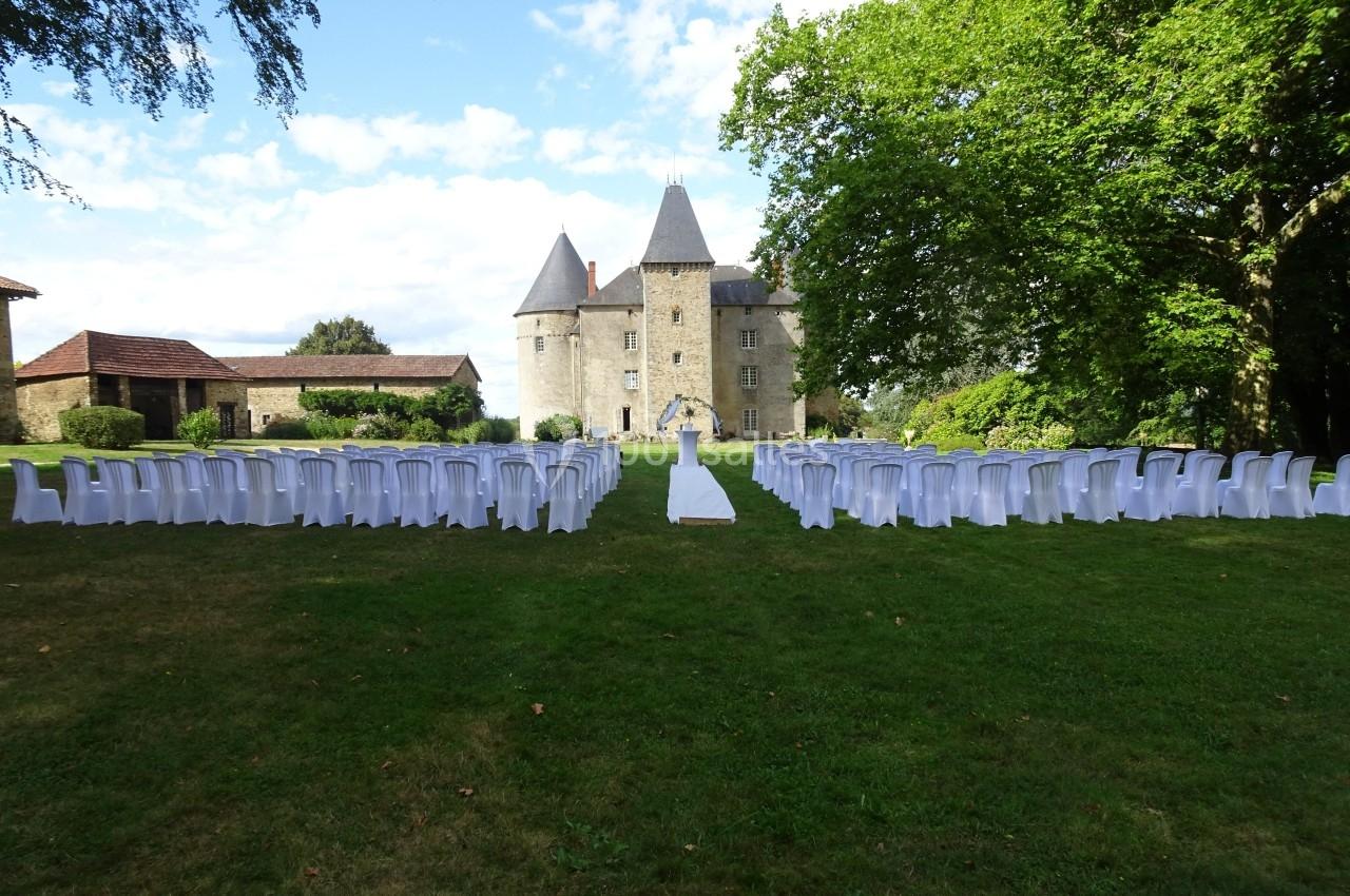 Chaises blanches disposées en rangées sur une pelouse face à un château, préparées pour une cérémonie en plein air.