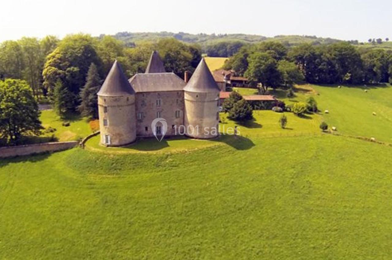 Vue aérienne d'un château entouré de tours rondes, situé dans un paysage verdoyant avec des prairies et des arbres.