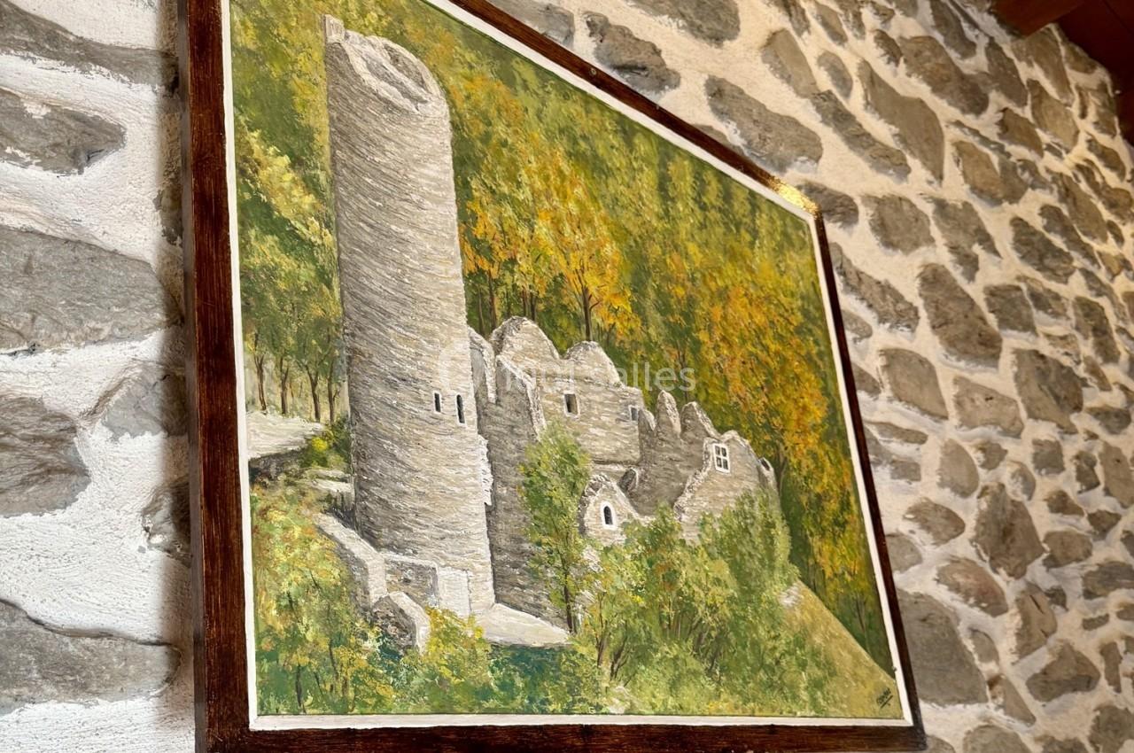 Peinture représentant des ruines en pierre entourées de végétation, accrochée sur un mur en pierre.