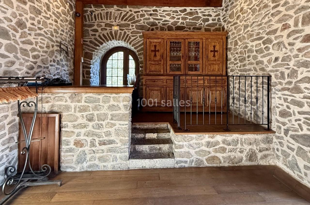 Intérieur en pierre avec un escalier menant à une mezzanine, meuble en bois massif et porte-fenêtre voûtée.