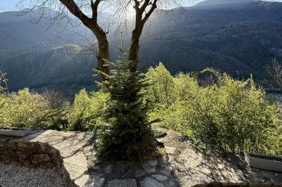 Terrasse en gravier avec parasols rouges, bordée d'un muret en pierre, offrant une vue sur des montagnes verdoyantes.