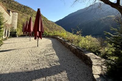 Terrasse en gravier avec parasols rouges, bordée d'un muret en pierre, offrant une vue sur des montagnes verdoyantes.