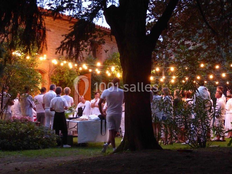 Groupe de personnes en tenue blanche rassemblées dans un jardin éclairé par des guirlandes lumineuses au crépuscule.