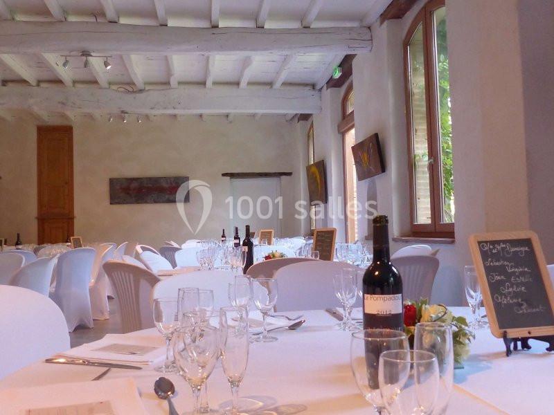 Salle lumineuse avec tables rondes dressées, nappes blanches, verres, bouteilles de vin et ardoises décoratives.