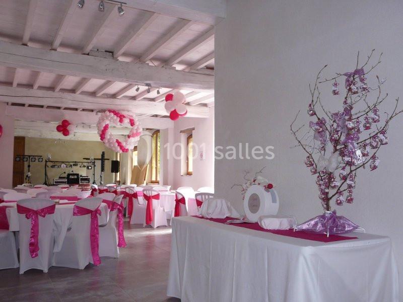 Salle de réception décorée en blanc et rose avec des tables dressées, des ballons et un arbre à dragées.