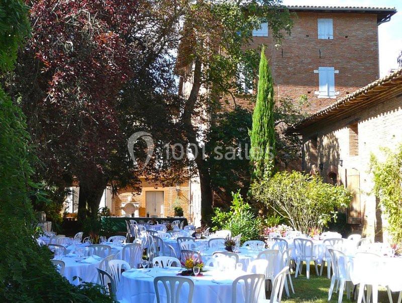 Jardin avec des tables rondes dressées pour un événement, entouré d'arbres et de bâtiments en briques.