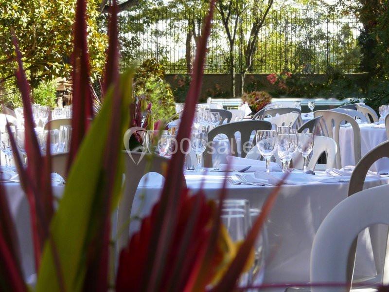 Tables dressées en extérieur avec nappes blanches, verres et couverts, entourées de végétation et de chaises blanches.