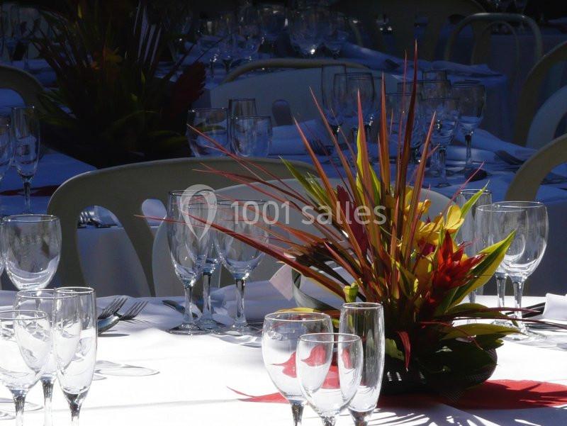 Centre de table floral coloré entouré de verres en cristal sur des tables dressées pour un événement.