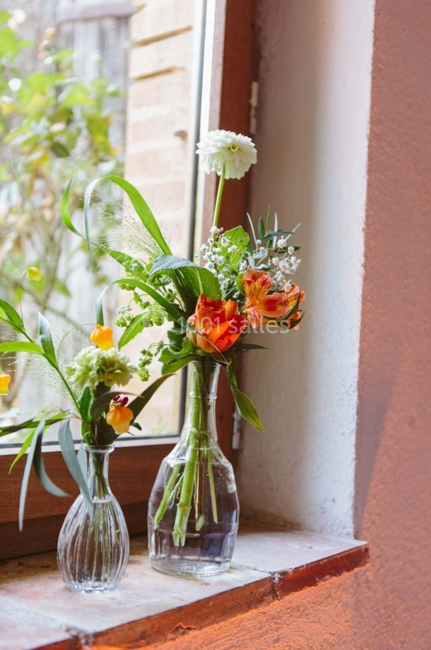 Deux vases en verre contenant des fleurs colorées, posés sur un rebord de fenêtre ensoleillé.