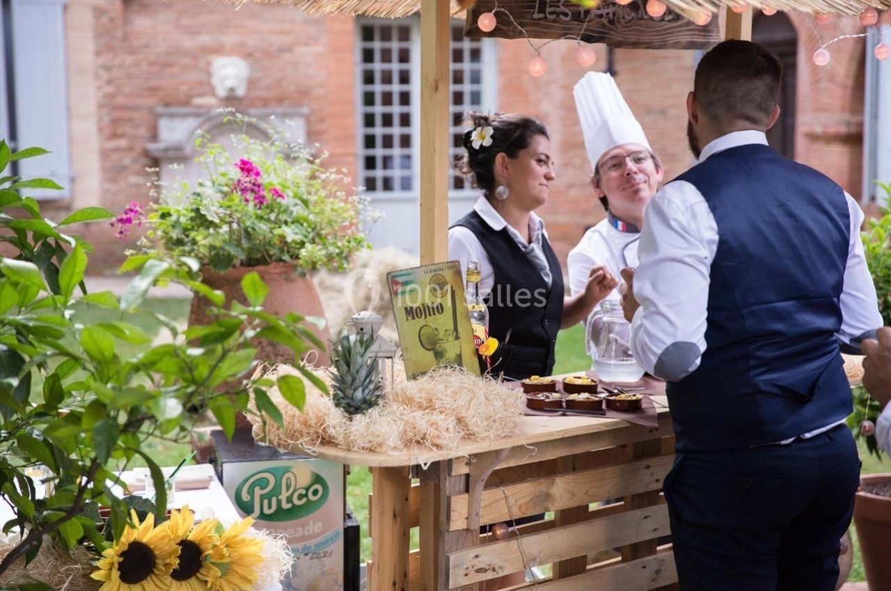 Un stand en bois décoré avec des boissons et des desserts, animé par un chef et deux serveurs en extérieur.