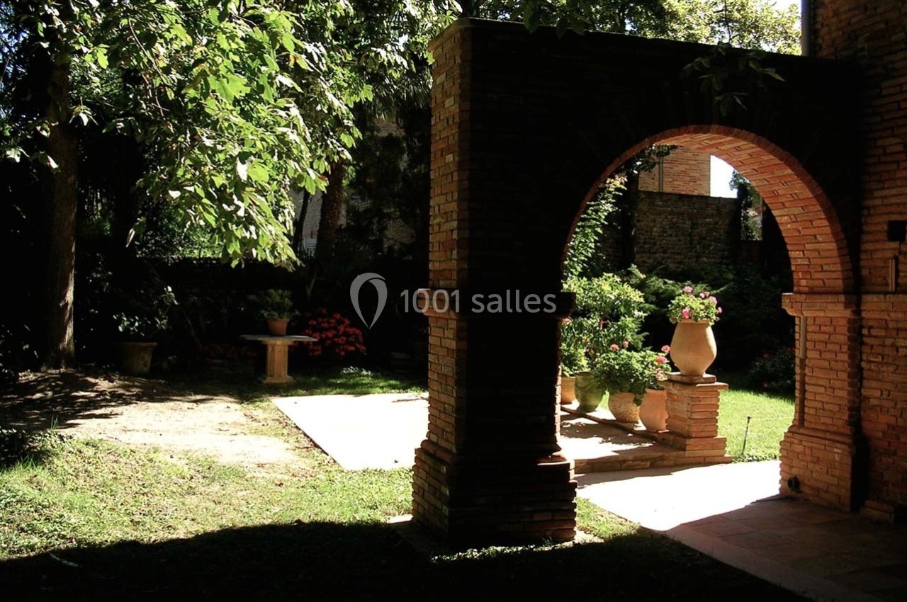Arc en briques dans un jardin ombragé avec des pots de fleurs et des arbres en arrière-plan.