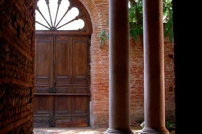 Entrée en briques rouges avec une porte verte ouverte et des lanternes suspendues à motifs zigzag.