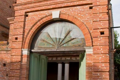 Entrée en briques rouges avec une porte verte ouverte et des lanternes suspendues à motifs zigzag.