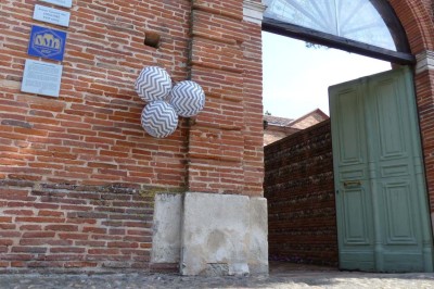 Entrée en briques rouges avec une porte verte ouverte et des lanternes suspendues à motifs zigzag.