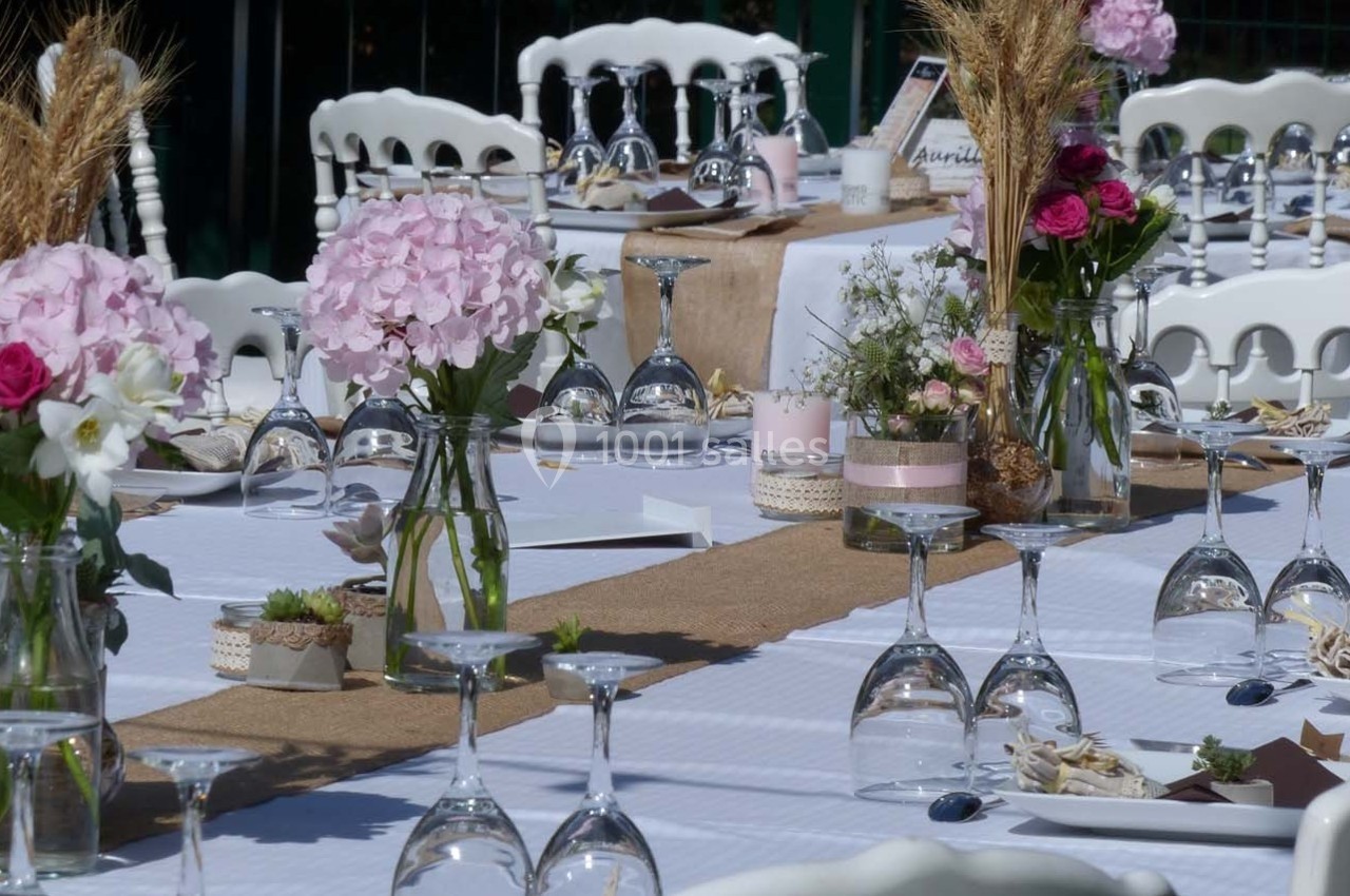 Tables décorées pour un événement avec nappes blanches, fleurs, verres retournés et chemins de table en toile de jute.