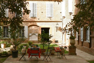 Entrée en briques rouges avec une porte verte ouverte et des lanternes suspendues à motifs zigzag.