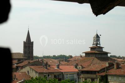 Vue sur les toits d'une ville avec un clocher en pierre et une tour en bois surmontée d'une cloche.