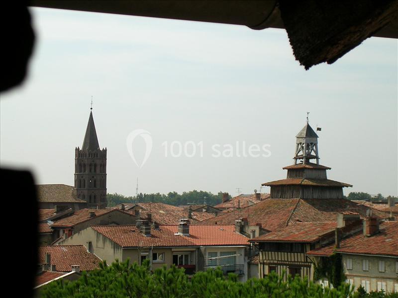 Vue sur les toits d'une ville avec un clocher en pierre et une tour en bois surmontée d'une cloche.