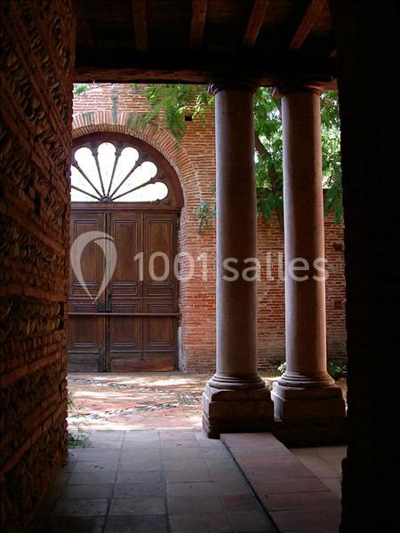 Vue d'un passage voûté en briques donnant sur une porte en bois avec un arc vitré et des colonnes en pierre.