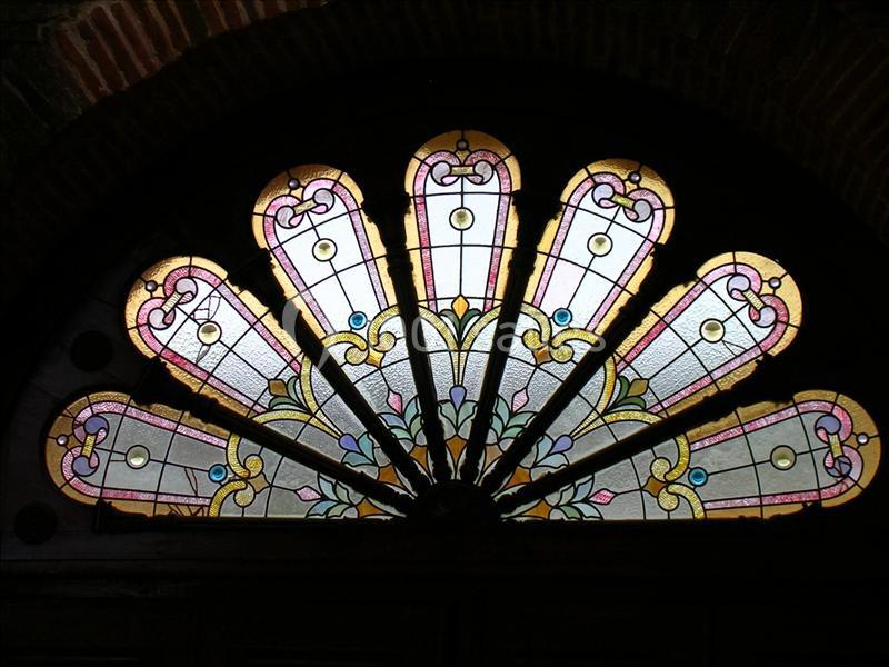 Vitrail en éventail avec motifs floraux et géométriques, encadré par une arche en briques sombres.