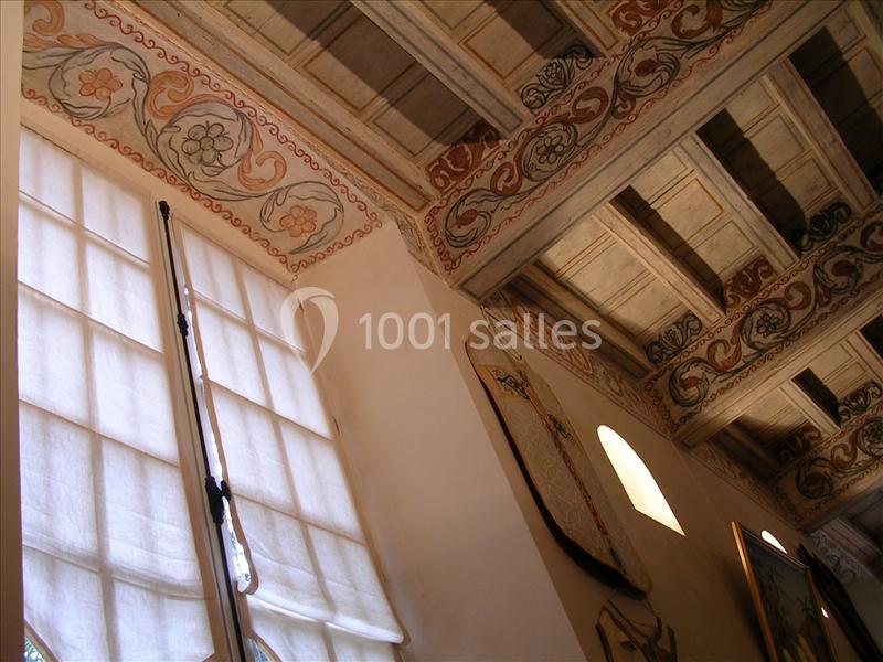 Plafond en bois décoré de motifs floraux et géométriques, avec des fenêtres aux rideaux translucides en dessous.