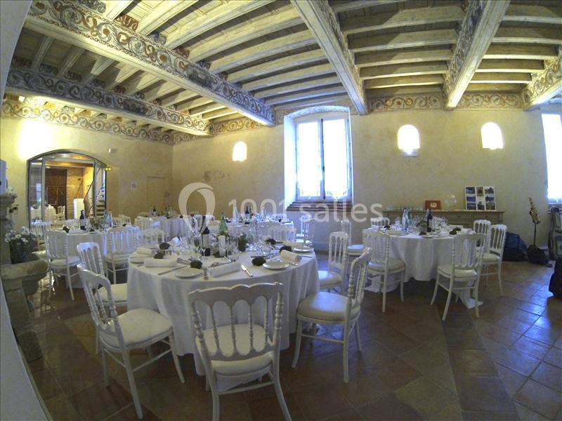 Salle de réception avec tables rondes dressées, chaises blanches et plafond en bois sculpté.
