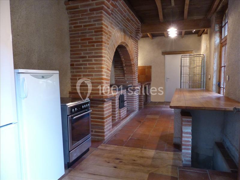 Cuisine rustique avec murs en briques, four intégré, réfrigérateur, cuisinière et plan de travail en bois.