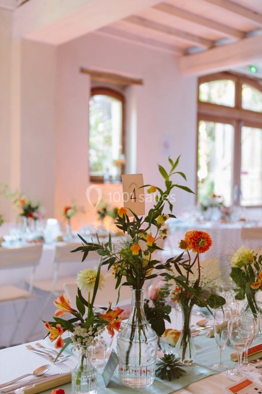 Décoration de table avec des fleurs colorées et un numéro de table ’4’ dans une salle lumineuse aux grandes fenêtres.