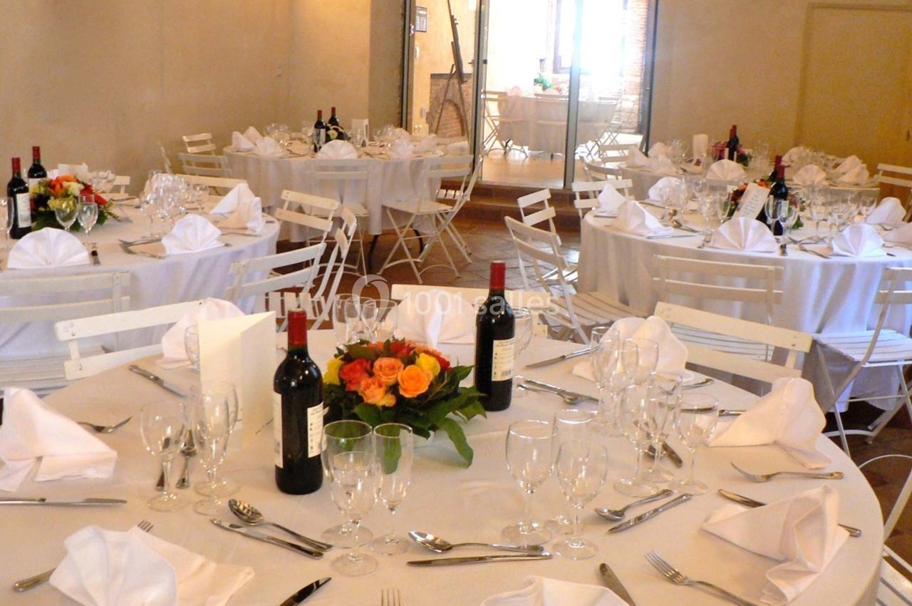 Tables rondes dressées pour un événement, avec nappes blanches, verres, couverts, bouteilles de vin et bouquets de fleurs.