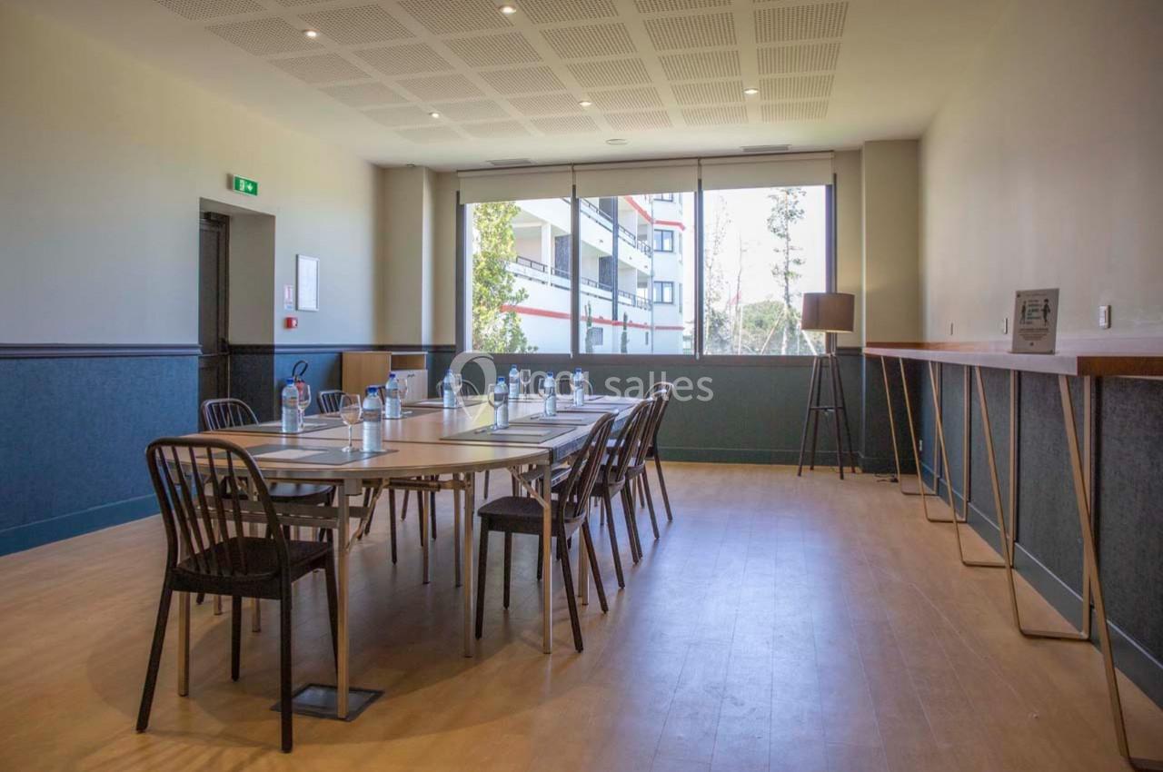 Salle de réunion lumineuse avec une grande table, des chaises, des bouteilles d'eau et une fenêtre donnant sur l'extérieur.