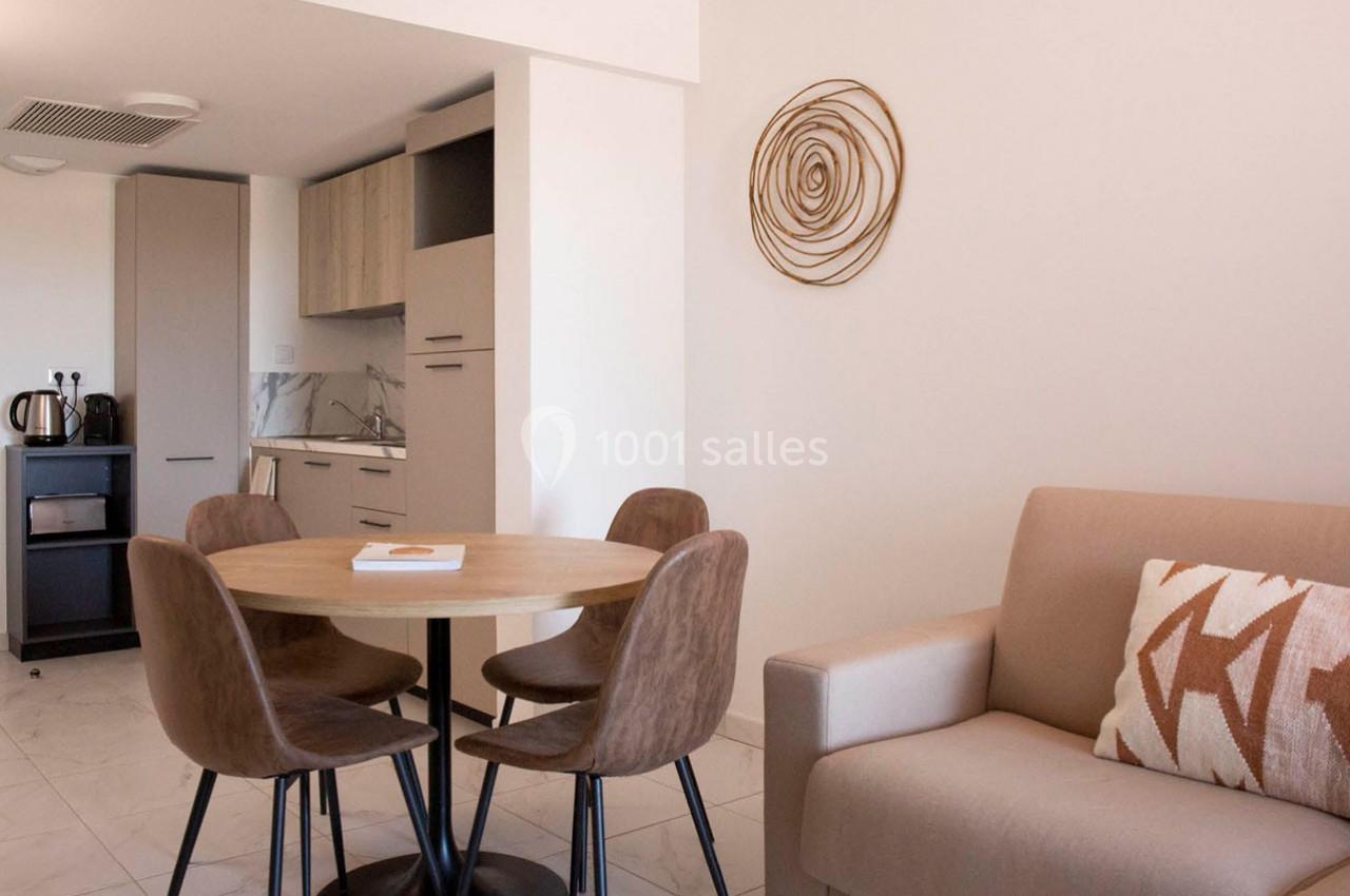 Salle à manger avec table ronde, quatre chaises, canapé beige, cuisine ouverte et décoration murale en spirale.