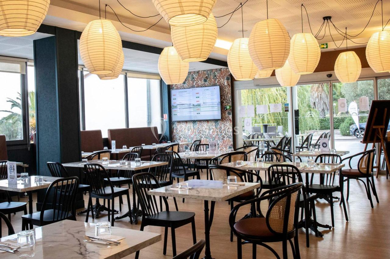 Salle de restaurant lumineuse avec tables en marbre, chaises noires et lampes suspendues en papier.