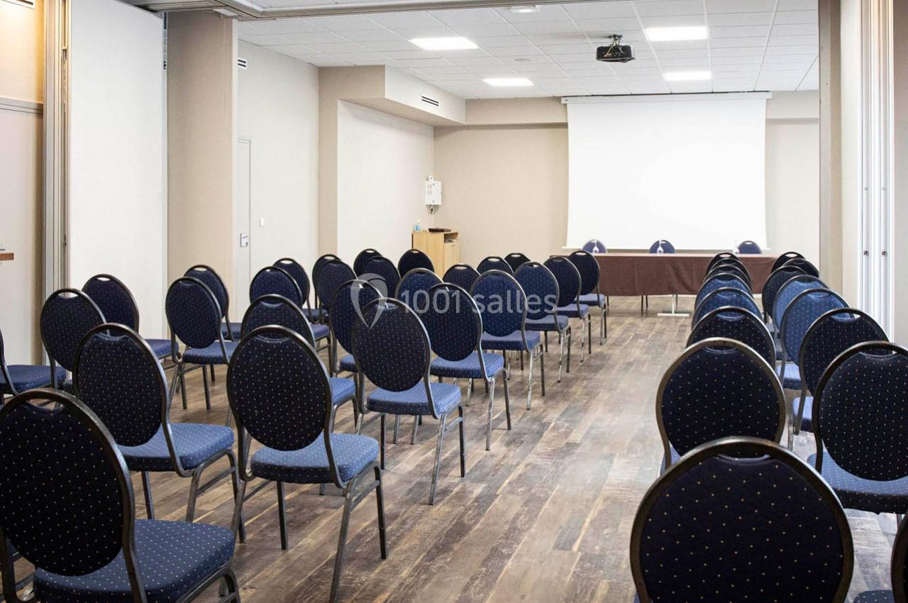 Salle de conférence vide avec des rangées de chaises bleues et un écran de projection blanc à l'avant.