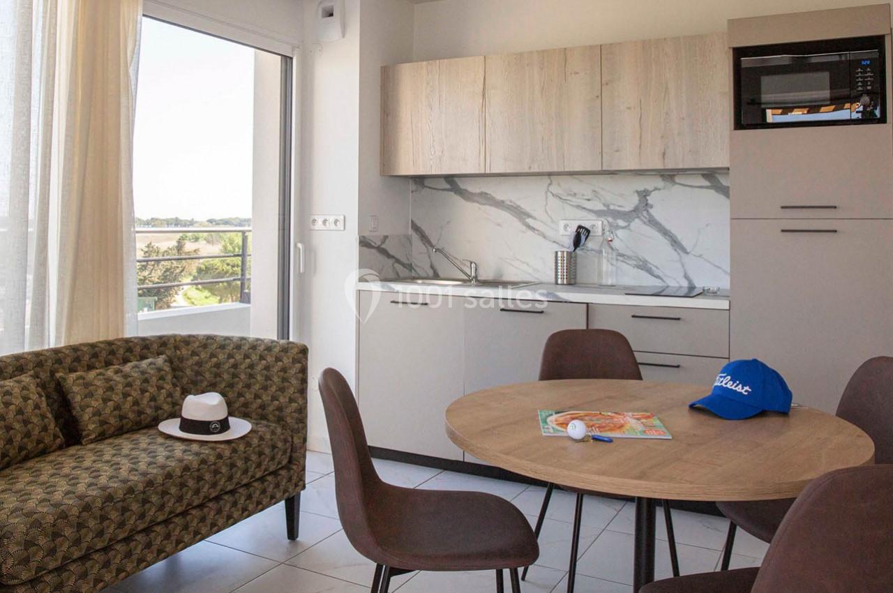 Cuisine ouverte avec table ronde, chaises, canapé, et vue sur un balcon, décorée d'objets du quotidien.