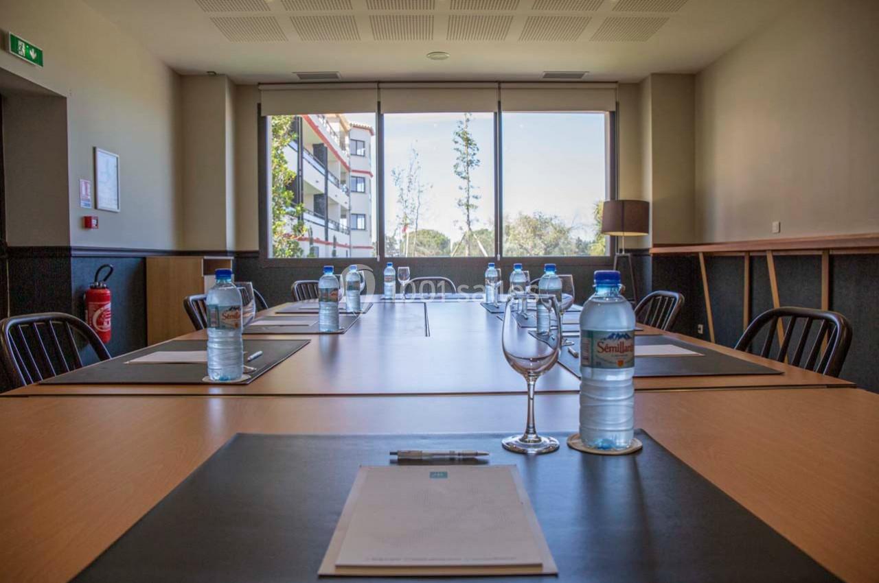 Salle de réunion lumineuse avec une grande table, des chaises, des bouteilles d'eau et des blocs-notes disposés.