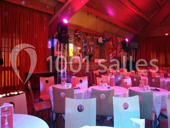 Salle de réception avec des tables rondes dressées, éclairage coloré et écrans suspendus.