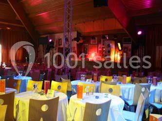 Salle de réception avec des tables rondes dressées, éclairage coloré et écrans suspendus.