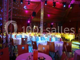 Salle de réception avec des tables rondes dressées, éclairage coloré et écrans suspendus.