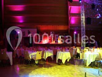 Salle de réception avec des tables rondes dressées, éclairage coloré et écrans suspendus.