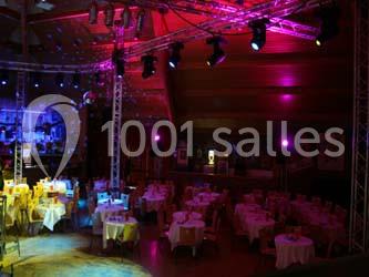 Salle de réception avec des tables rondes dressées, éclairage coloré et écrans suspendus.