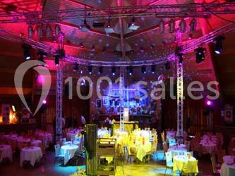 Salle de réception décorée avec des tables rondes, éclairages colorés et une scène équipée de projecteurs.
