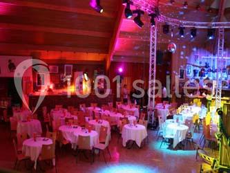 Salle de réception avec des tables rondes dressées, éclairage coloré et écrans suspendus.